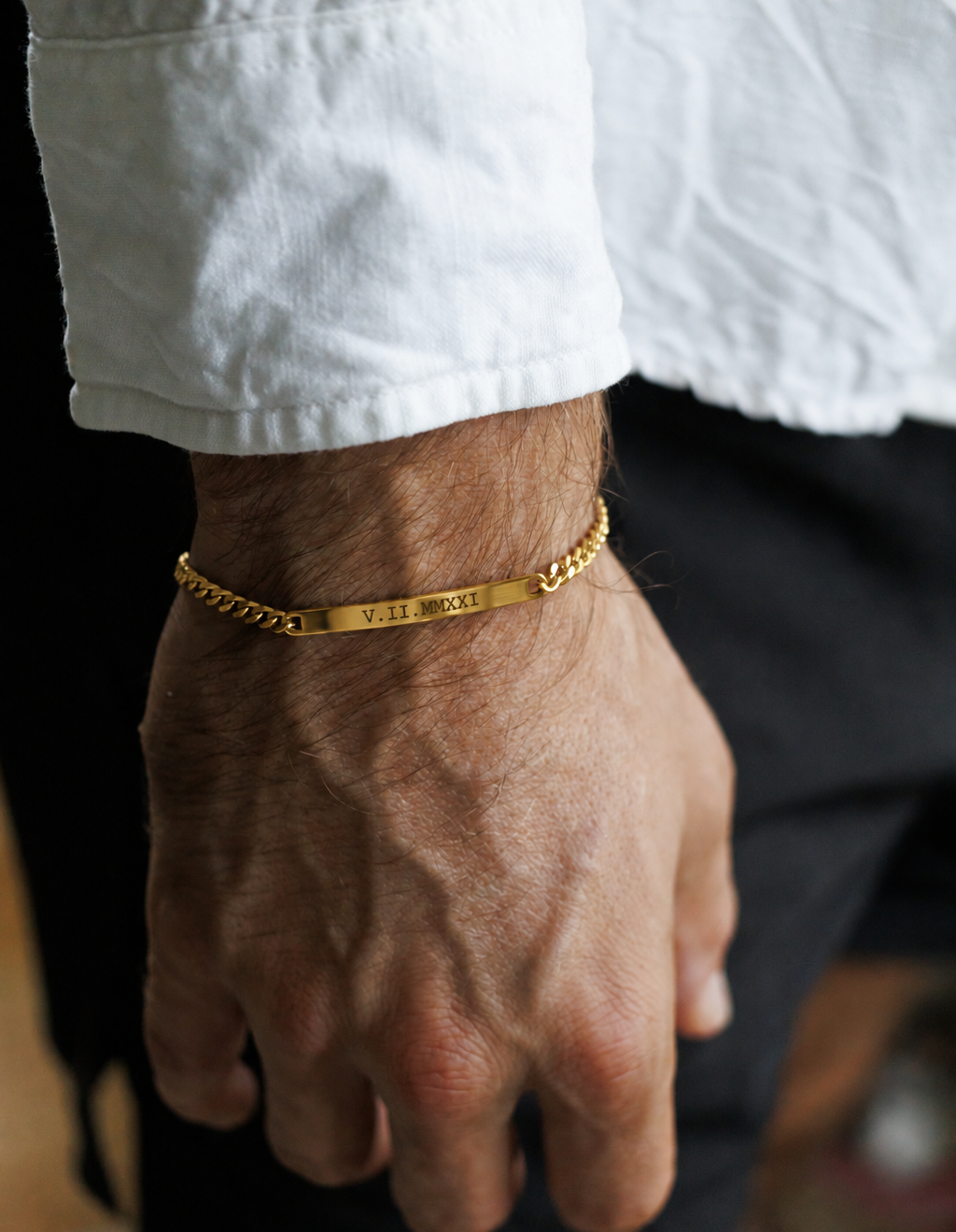 A close-up of a man's hand and wrist wearing a gold chain bracelet with engraved text.